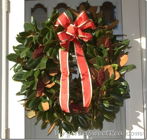 Magnolia wreath decorated for Christmas with a red ribbon and sumac berries.