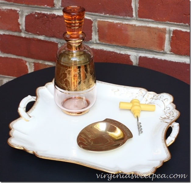Haviland platter displayed with a vintage decanter, wine cork, and brass plate. 