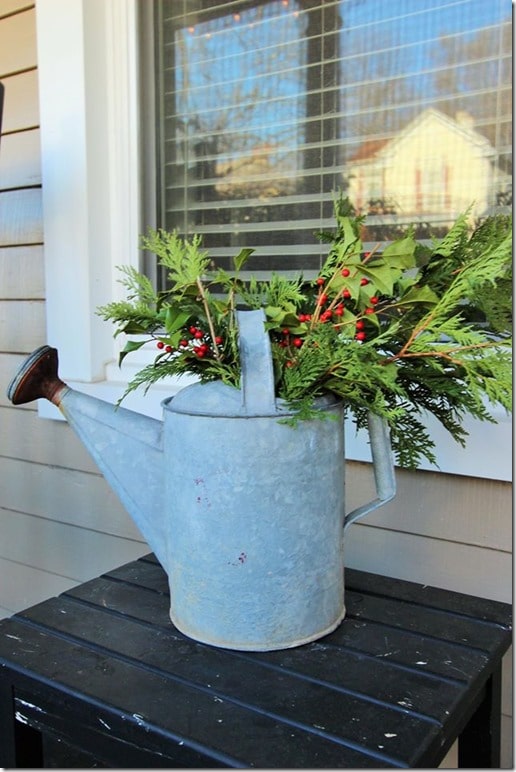 Fresh greenery looks pretty in a watering can as Christmas decor on a porch.