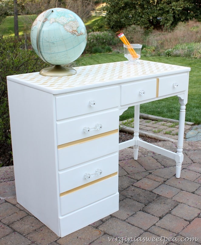 A made over desk with white and gold paint and glass knobs.  