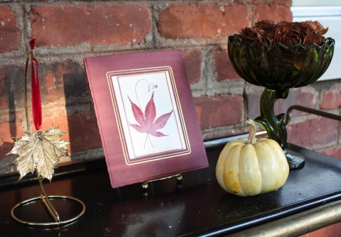 Fall Decor including a pressed maple leaf, gold maple leaf, pumpkin, and pine cones that look like roses.