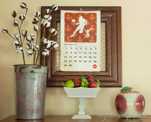 Fall Vignette with a 1968 Coca-Cola Calendar, McCoy Apple Cookie Jar, and Cotton Stems in a Sap Bucket.