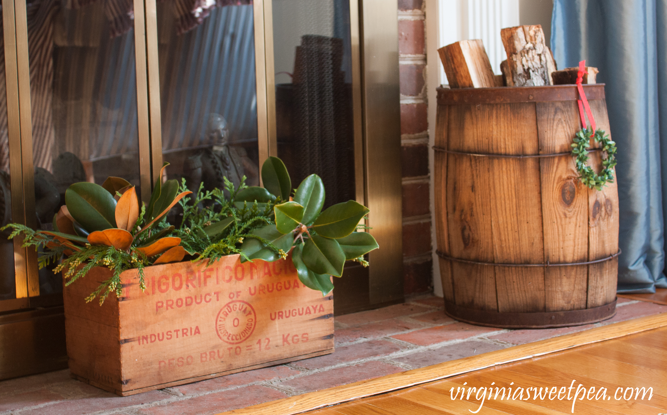 Christmas Hearth - A vintage box filled with greens along with a wooden barrel filled with logs grace the hearth for Christmas. #christmas #christmashomedeco #christmasideas #favoritechristmasideas #vintagechristmas