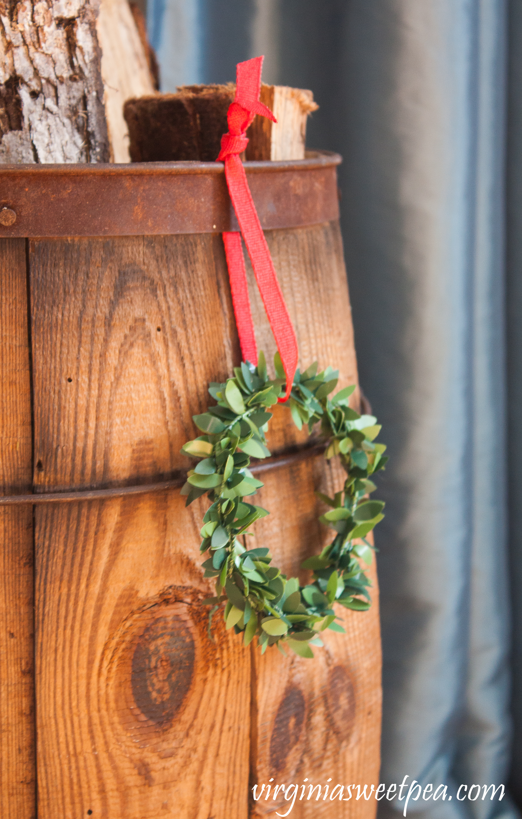 A vintage wooden barrel filled with logs is embellished with a boxwood wreath for Christmas. #christmas #christmashomedecor #christmasideas #favoritechristmasideas #vintagechristmas