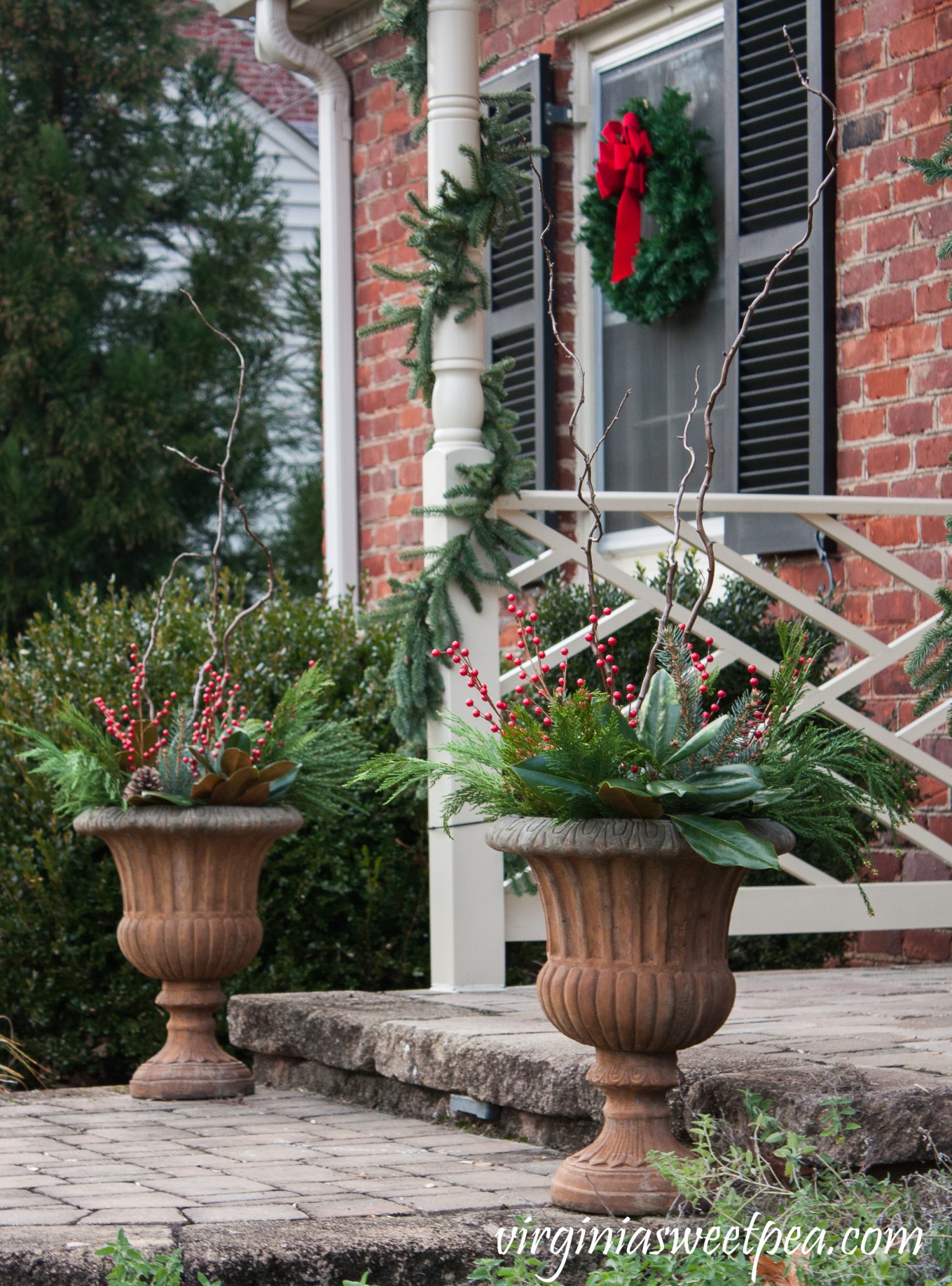 Front porch urns decorated with fresh greenery, curly willow branches and faux berries.