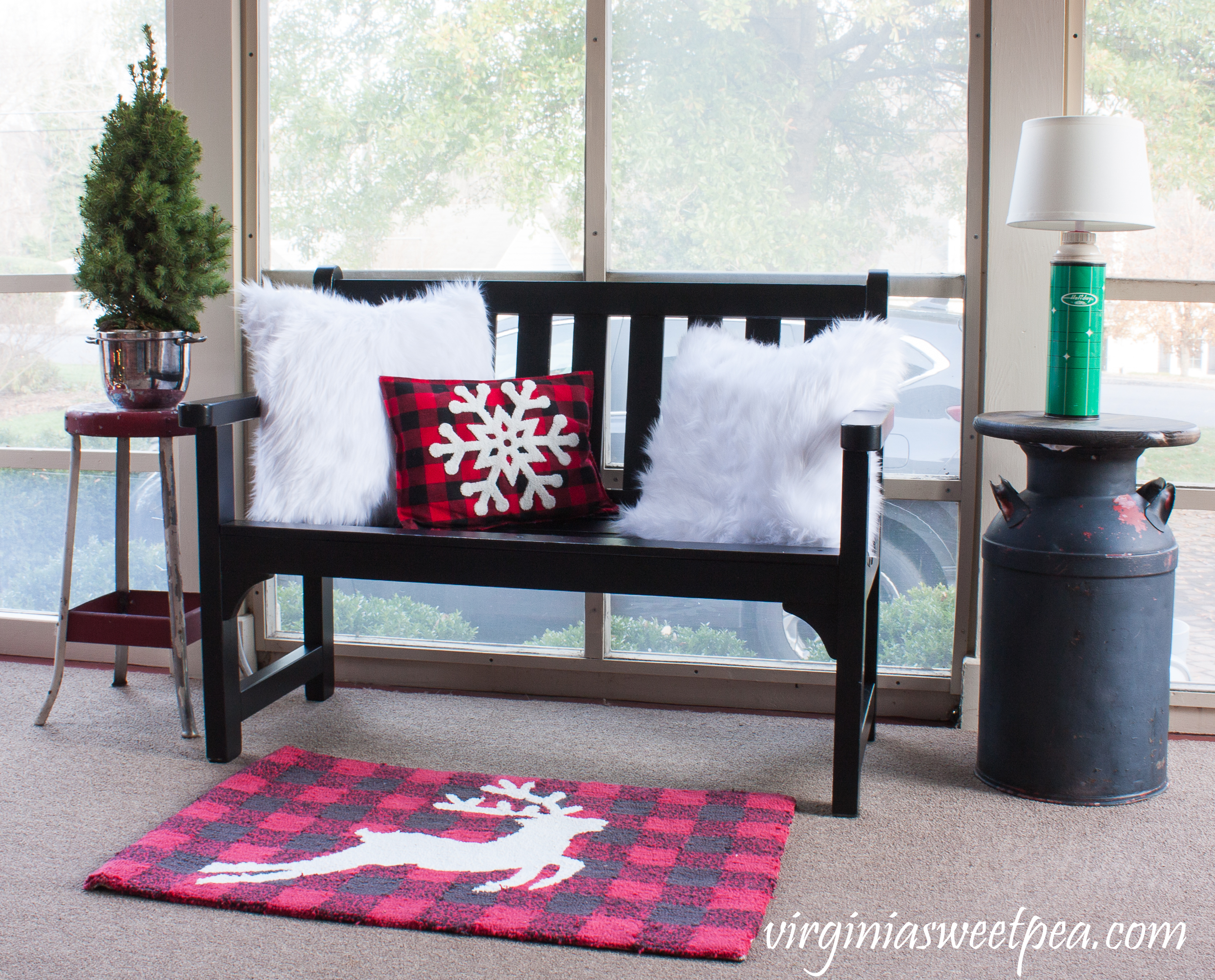 Christmas Porch Decor - A black bench filled with Christmas pillows is flanked by a vintage metal stool with a tree planted in a vintage silver ice bucket along with a vintage milk can topped with a lamp made from a vintage thermos. #christmas #christmasdecorations #christmasporch #vintage #vintagechristmas