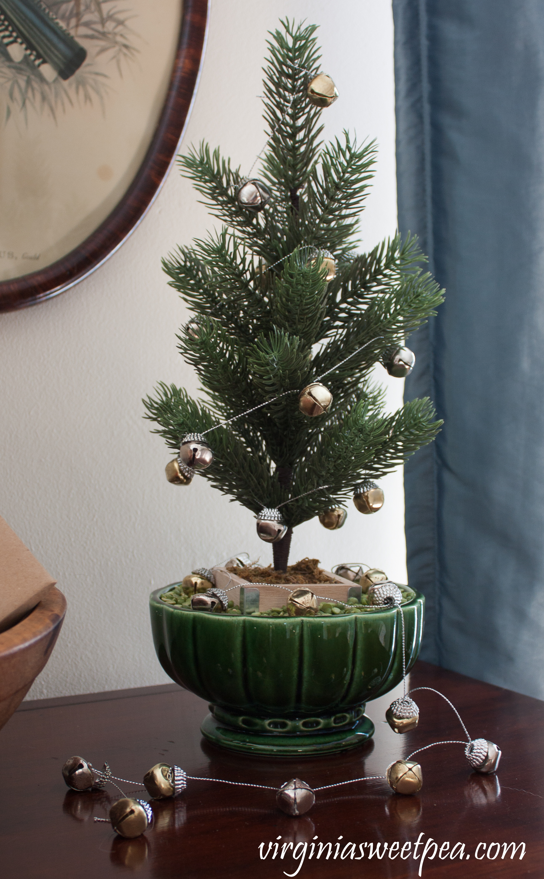 Christmas Home Tour - A small tree is "planted" in a vintage planter with split peas used for soil and decorated with a bell garland. #christmas #christmastree #christmasdecorations