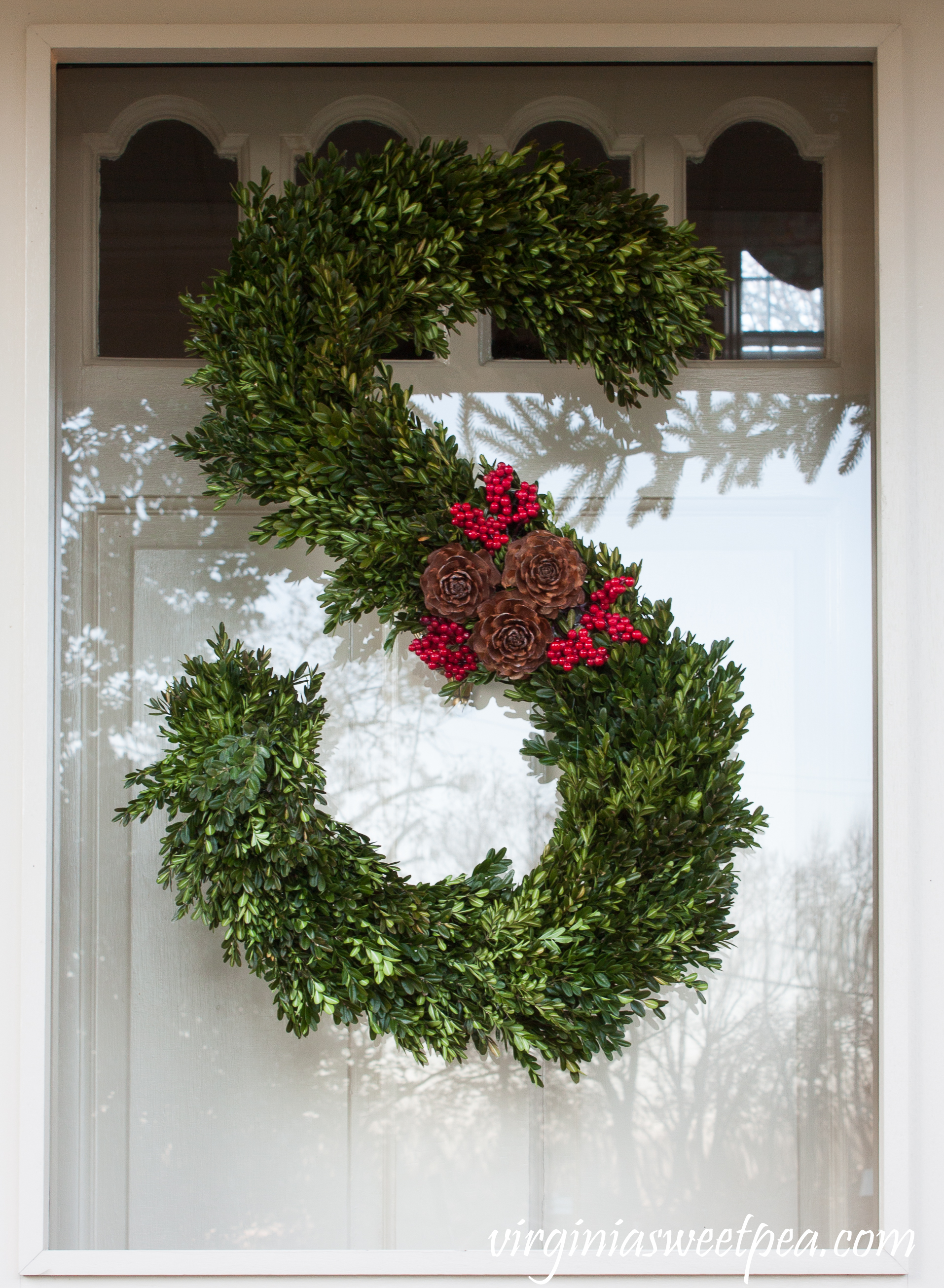 Front porch decorated for Christmas with a handmade monogram wreath decorated with boxwood, berries, and pinecones.