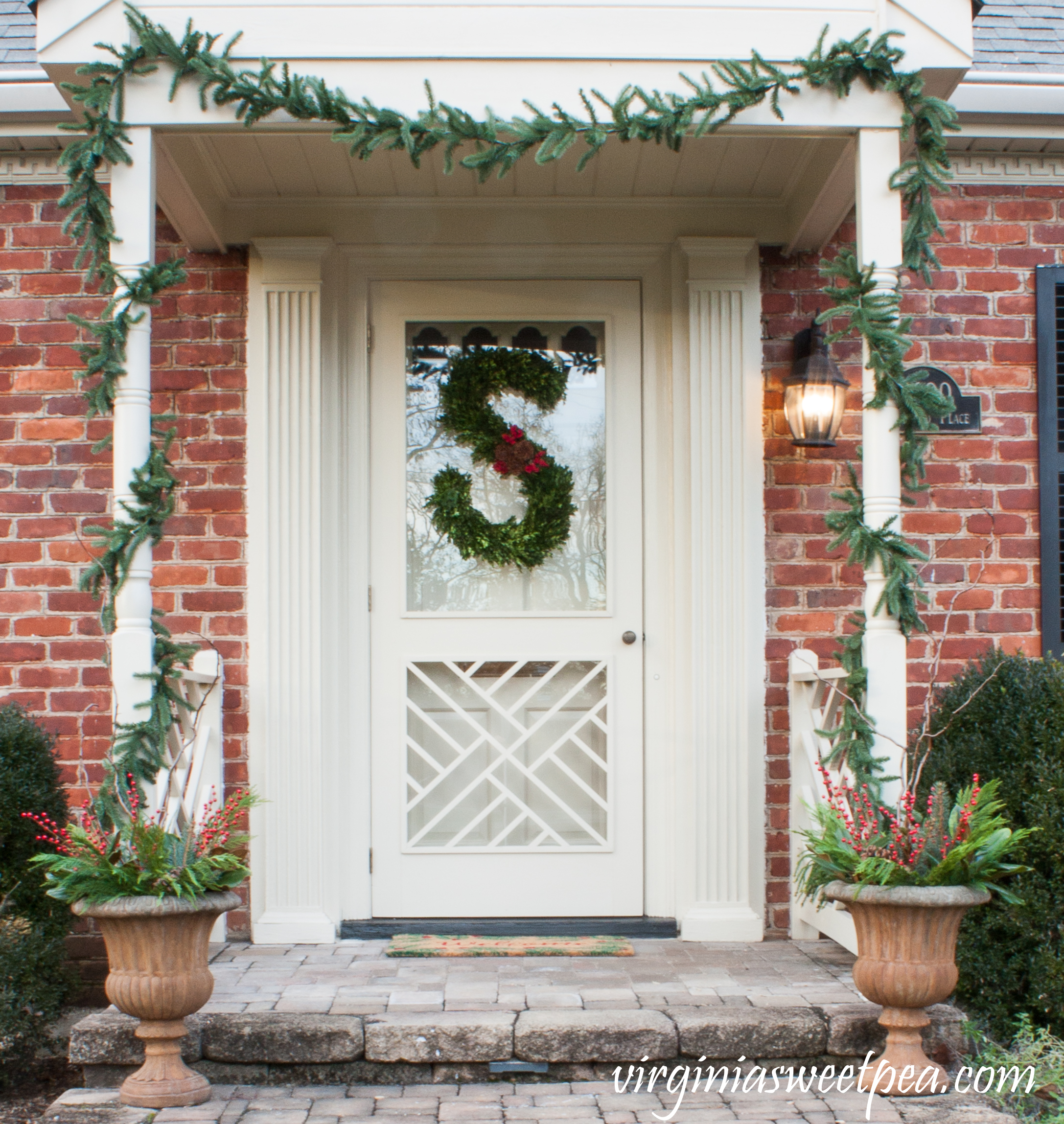Front porch decorated for Christmas with a handmade monogram wreath decorated with boxwood, berries, and pinecones.