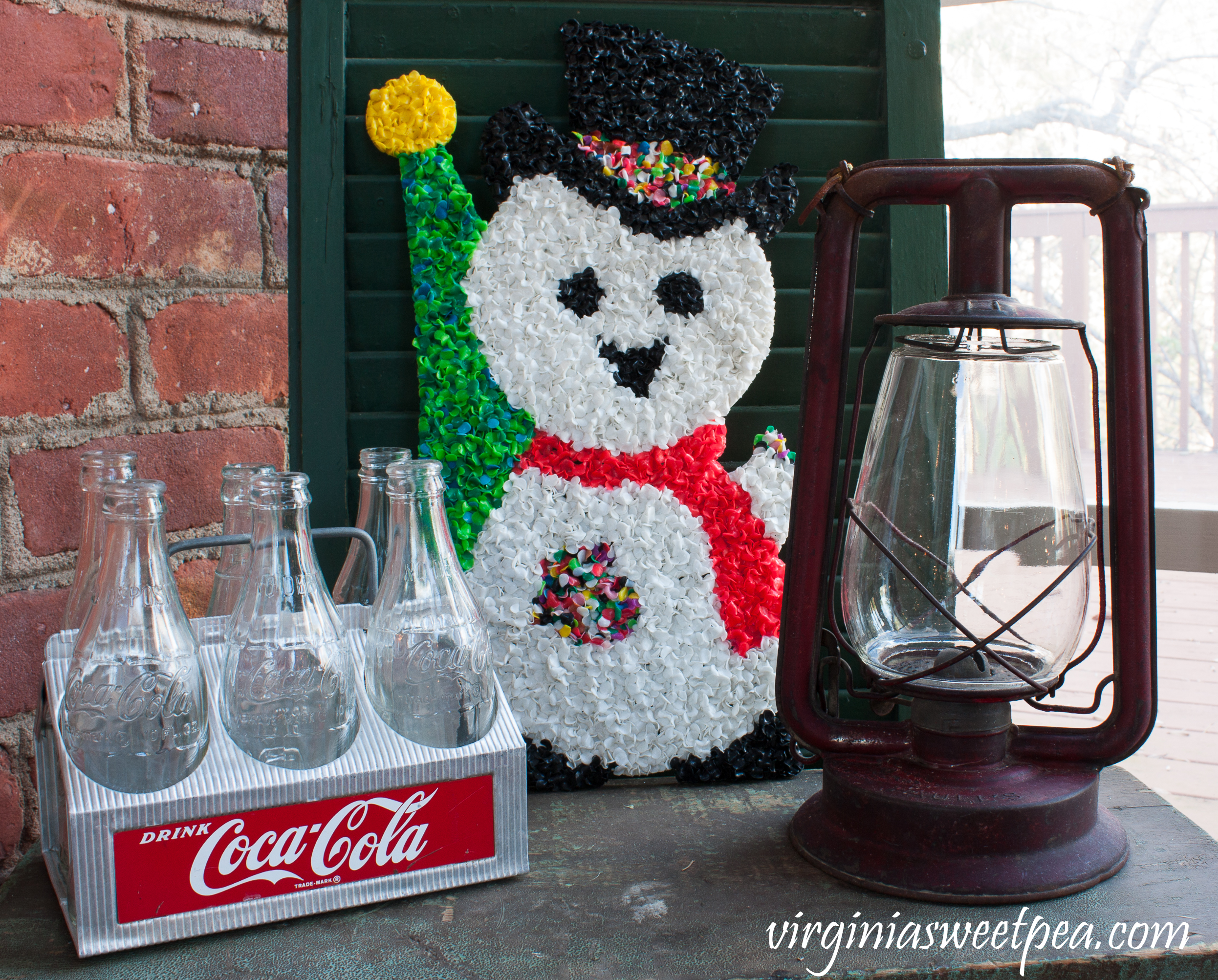 Vintage Christmas Vignette - A Coke caddy, 1970's plastic snowman door decor, and an antique lantern are displayed on a an antique tool chest. #christmas #christmasdecorations #christmastree #christmasporch #vintagechristmas #cocacola