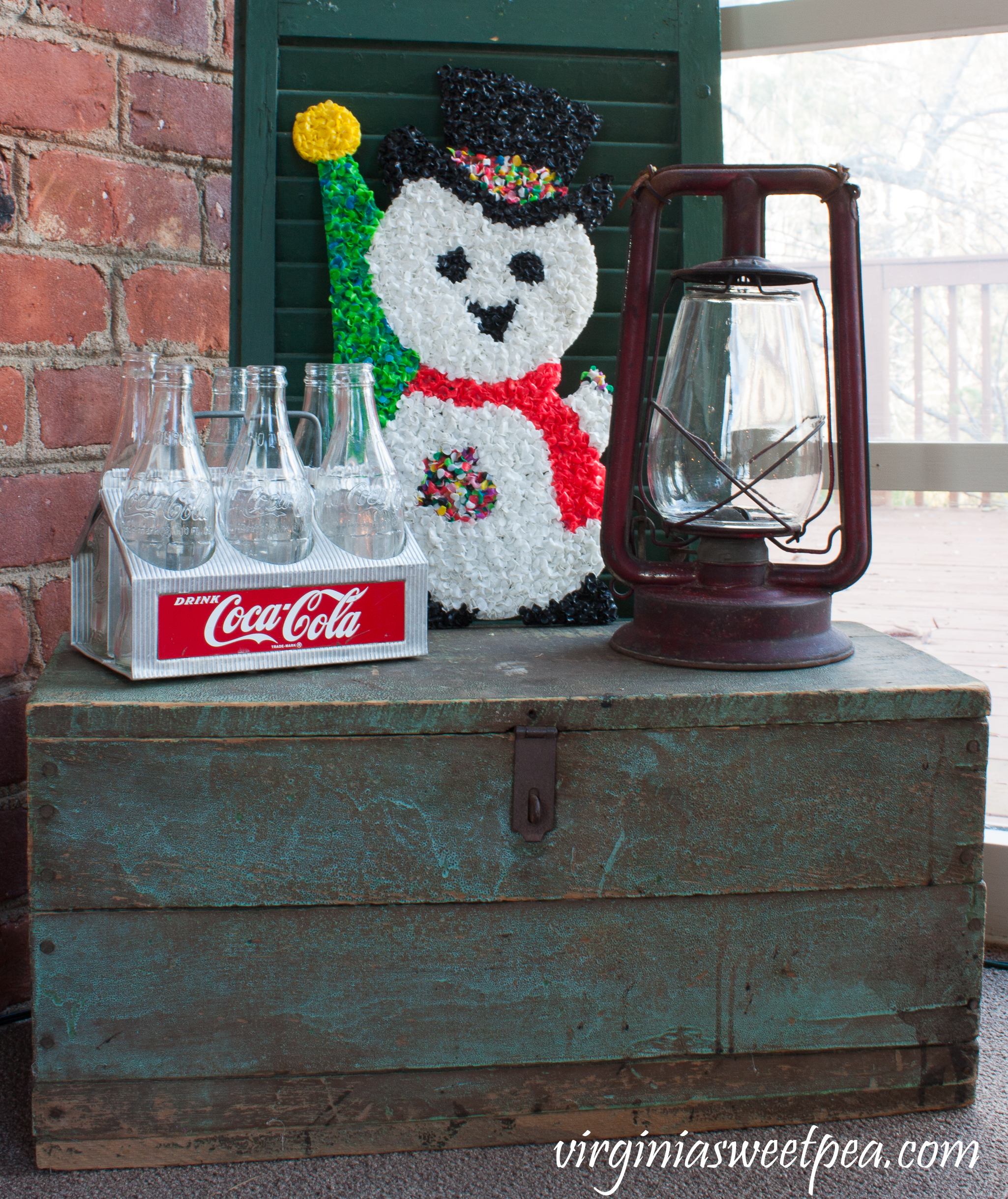 Vintage Christmas Vignette - A Coke caddy, 1970's plastic snowman door decor, and an antique lantern are displayed on a an antique tool chest. #christmas #christmasdecorations #christmastree #christmasporch #vintagechristmas #cocacola