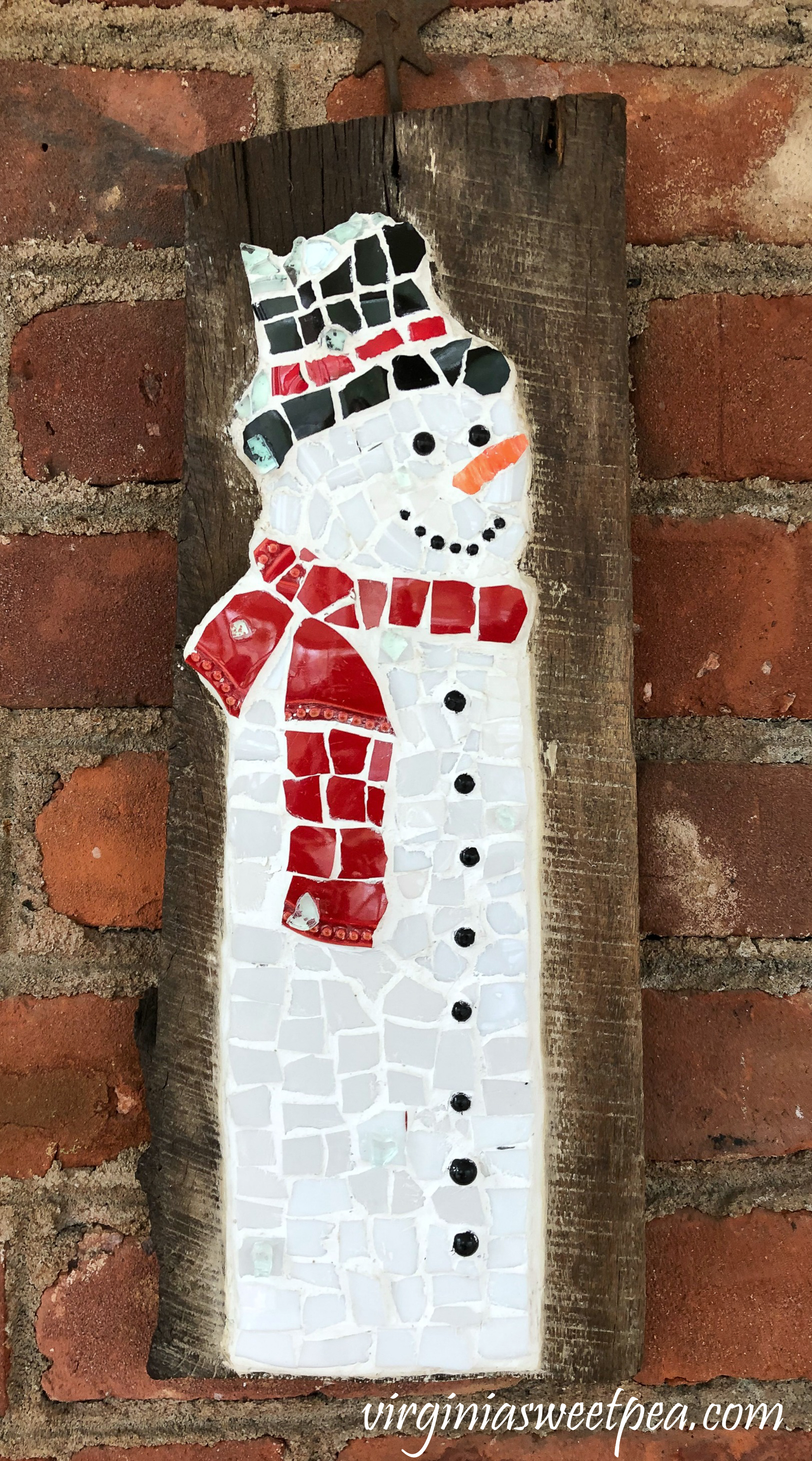 Snowman made with dish pieces on a piece of barnwood. 