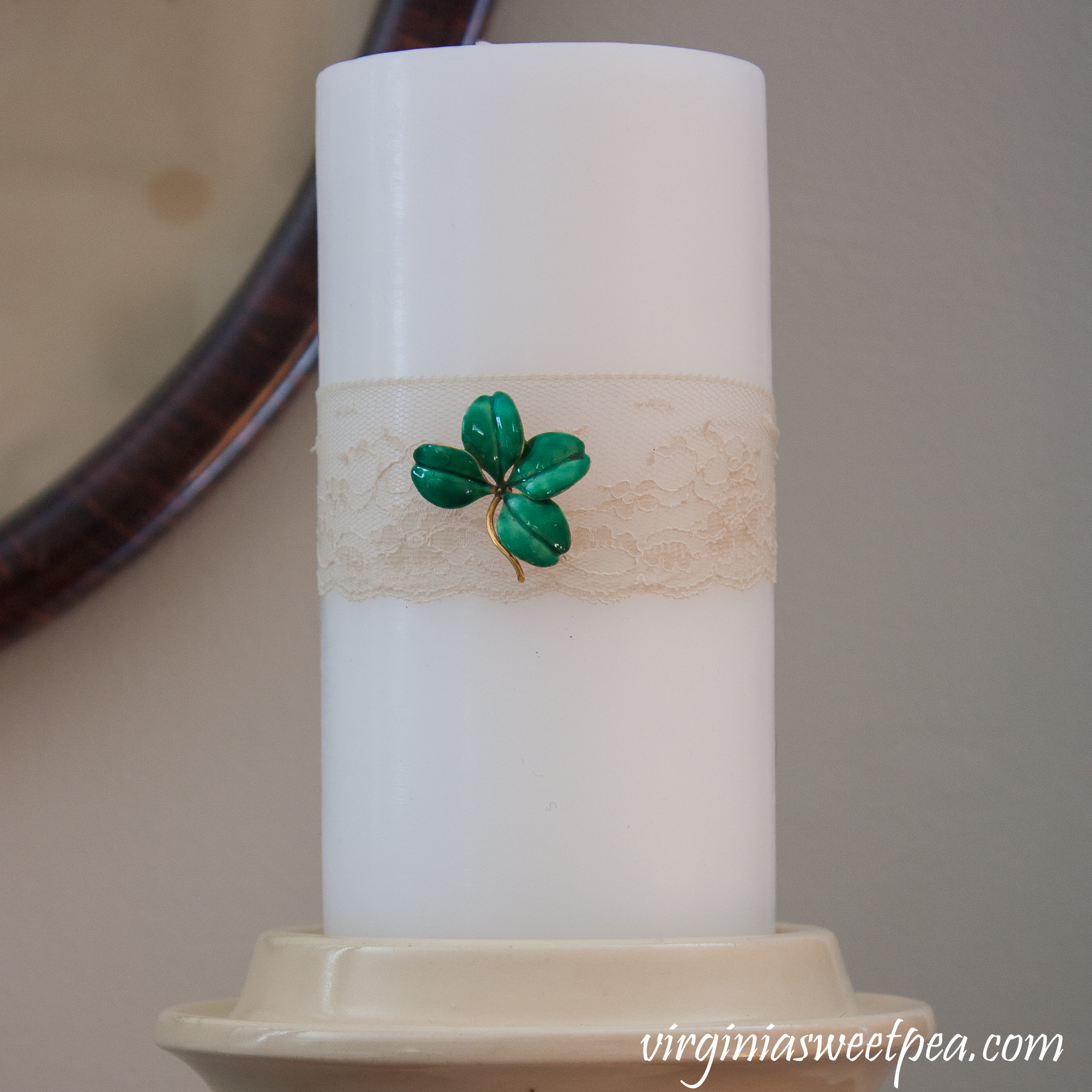 Candle decorated for St. Patrick's Day with lace and a vintage four leaf clover pin. #stpatricksdaydecor #vintagejewelry #fourleafcloverpin