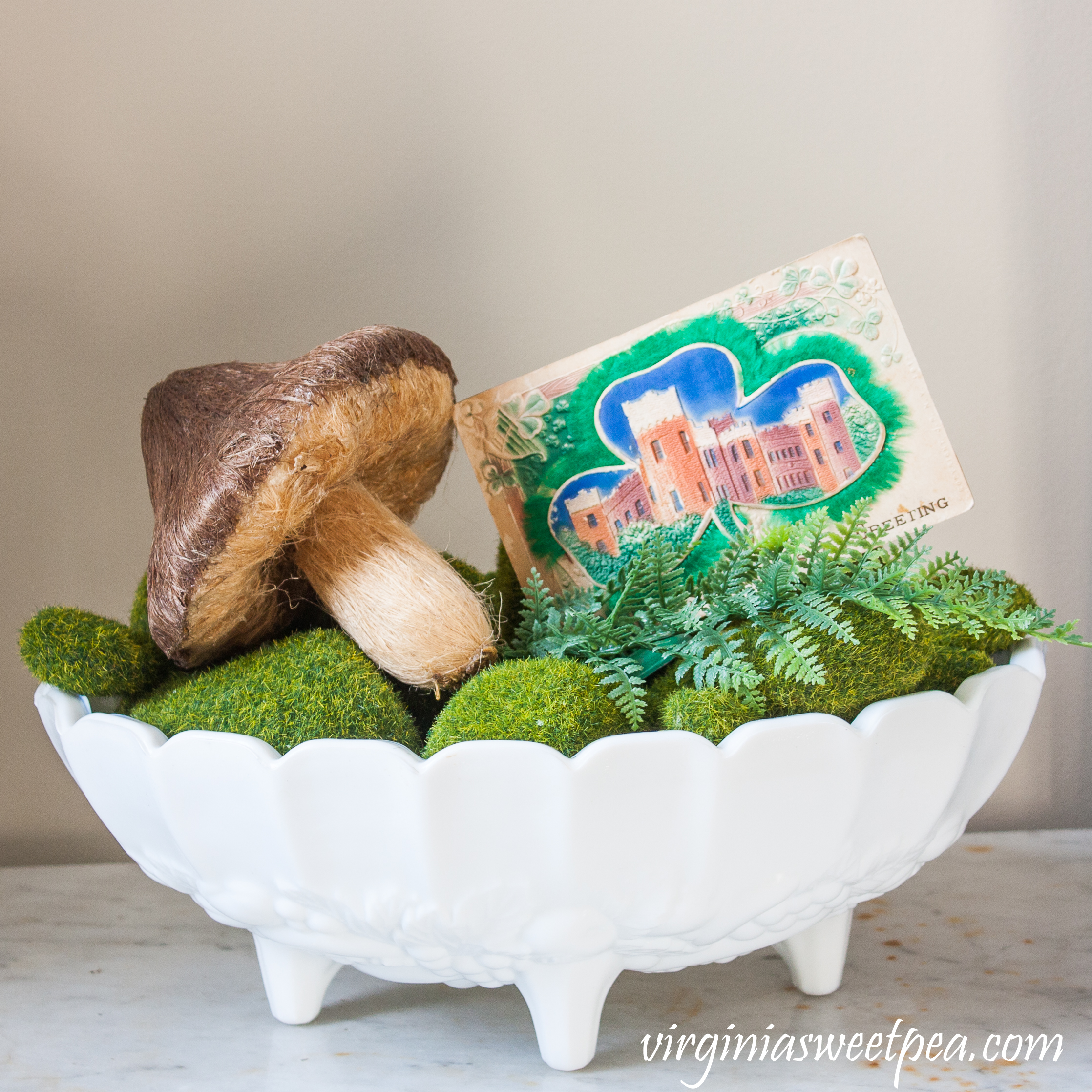 St. Patrick's Day vignette in a milk glass compote with faux moss stones, a faux mushroom, and a vintage St. Patrick's Day postcard. #stpatricksday #stpatricksdaydecor #vintagedecor