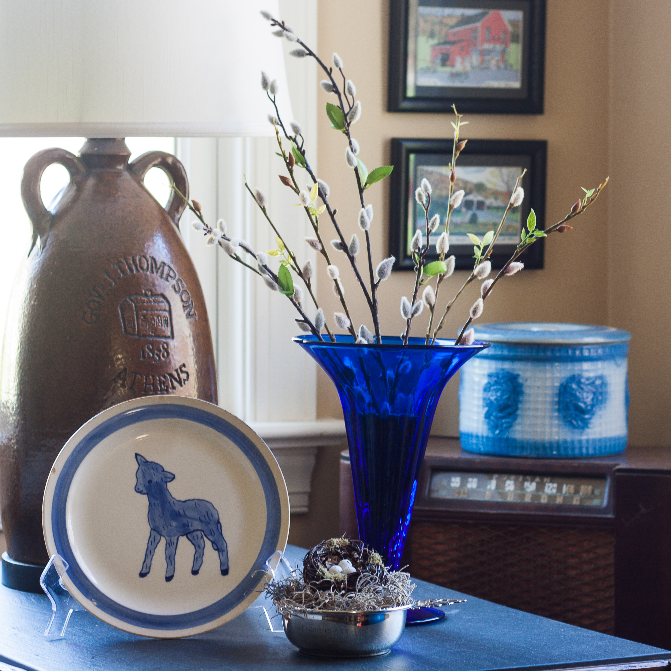 Easter vignette with a Blue Ridge Pottery lamb plate, Blenko blue vase, and a silver child's porridge bowl with a nest.