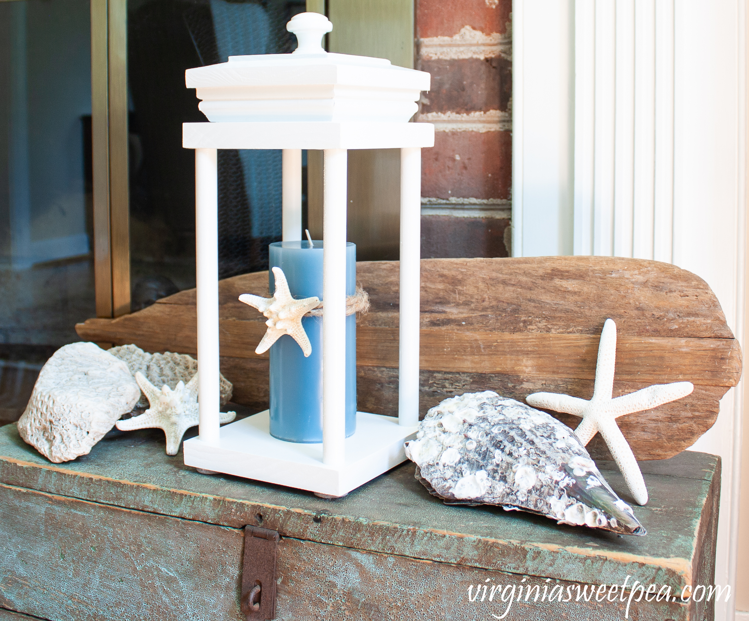 Coastal themed summer vignette with a lantern, shells, coral, and an old wooden oar.