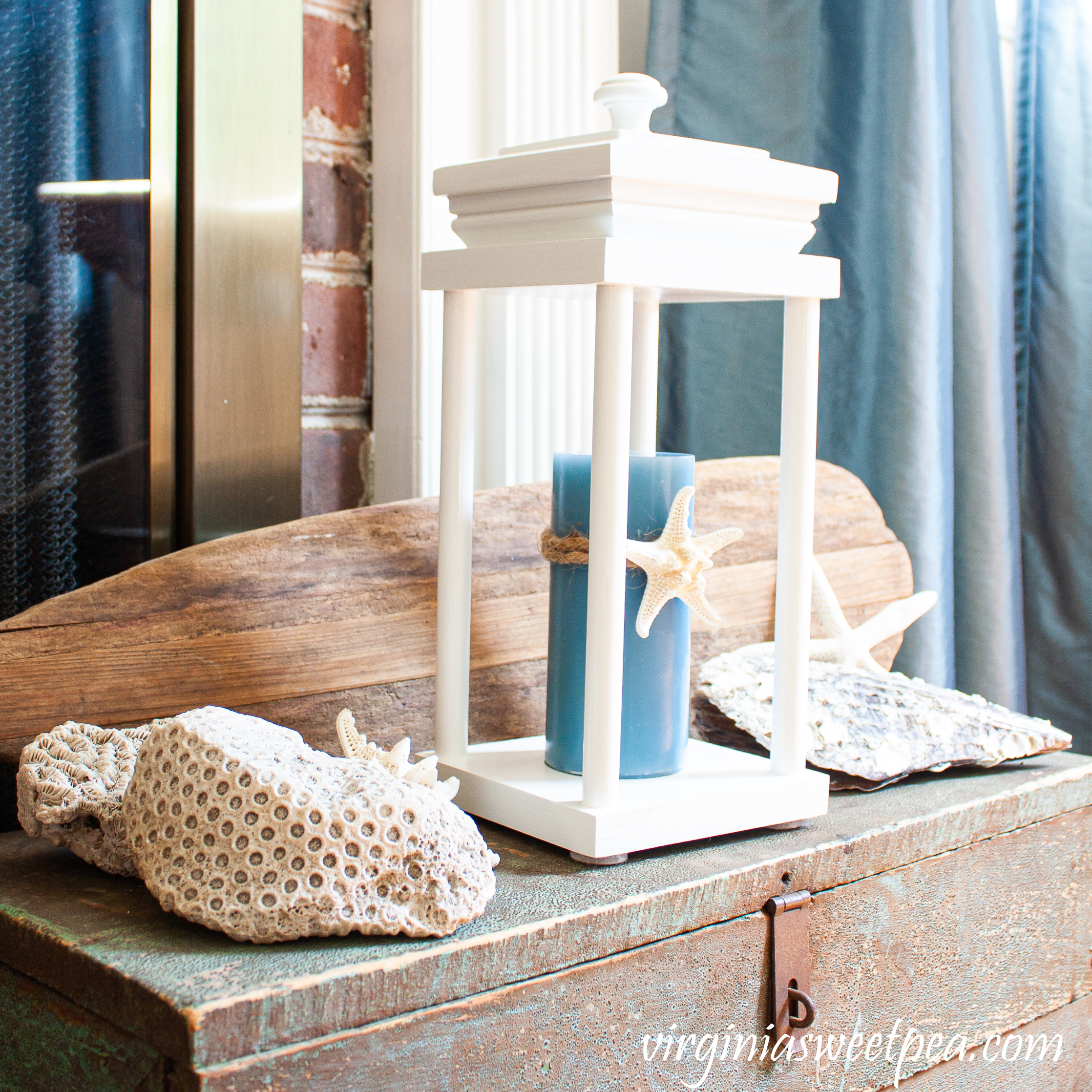 Coastal themed summer vignette with a lantern, shells, coral, and an old wooden oar.