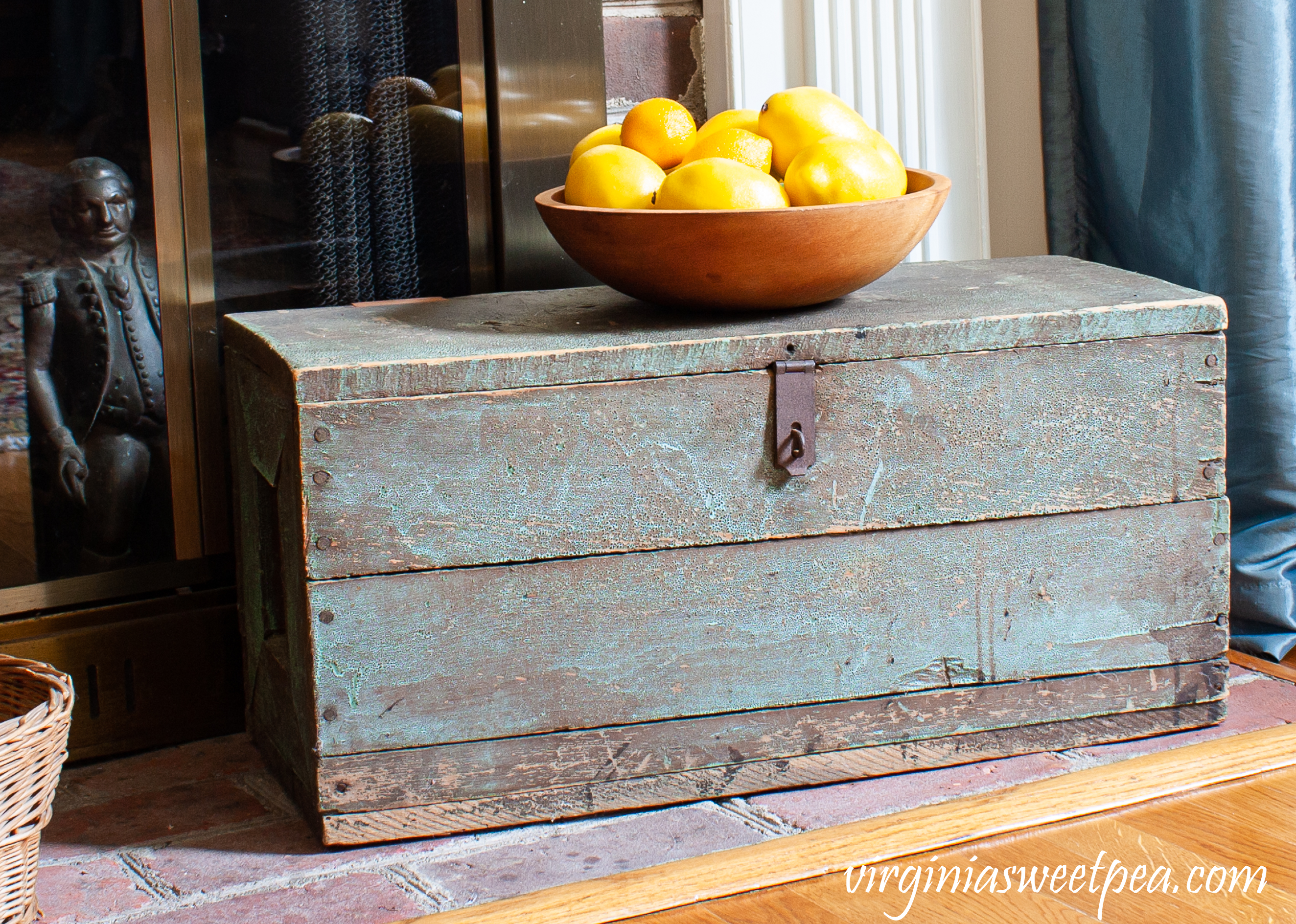 Antique tool box on a fireplace hearth with a wooden bowl filled with lemons.