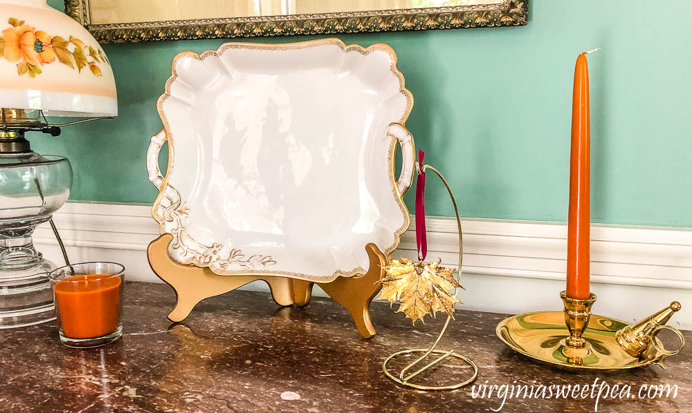 Fall vignette with a Haviland platter, gold preserved Vermont maple leaf ornament, brass candle holder, and an IKEA candle