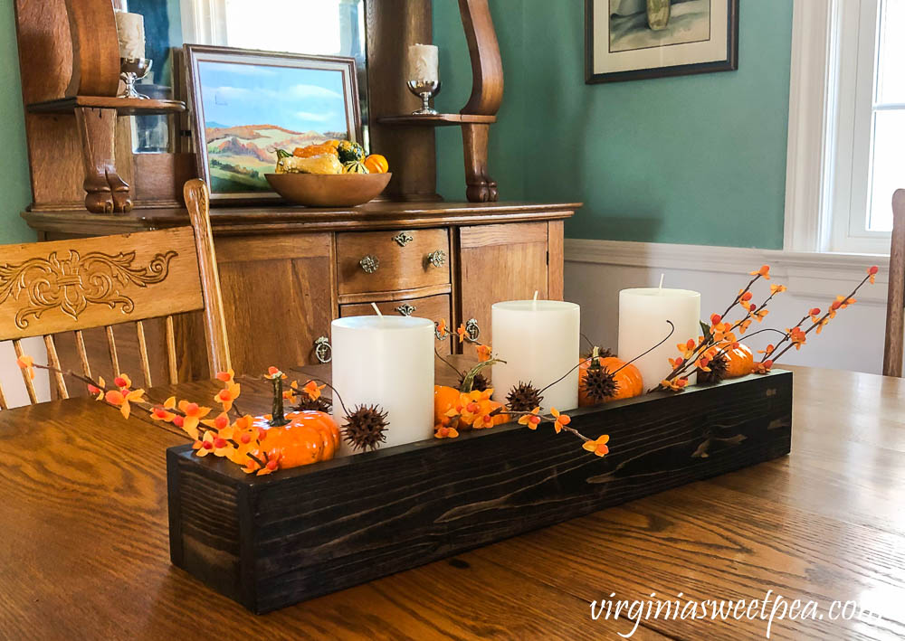 A DIY wood box filled with candles, pumpkins, bittersweet, and sweet gum balls is used as a table centerpiece.