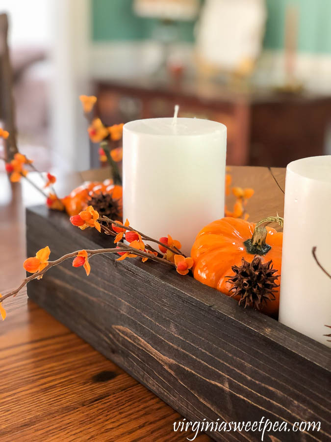 A DIY wood box filled with candles, pumpkins, bittersweet, and sweet gum balls is used as a table centerpiece.