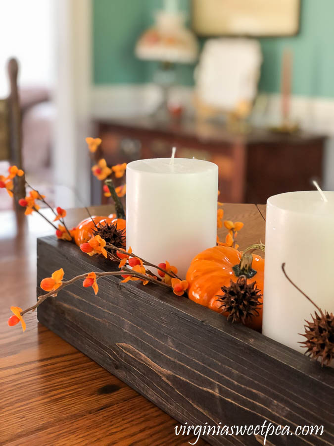 A DIY wood box filled with candles, pumpkins, bittersweet, and sweet gum balls is used as a table centerpiece.