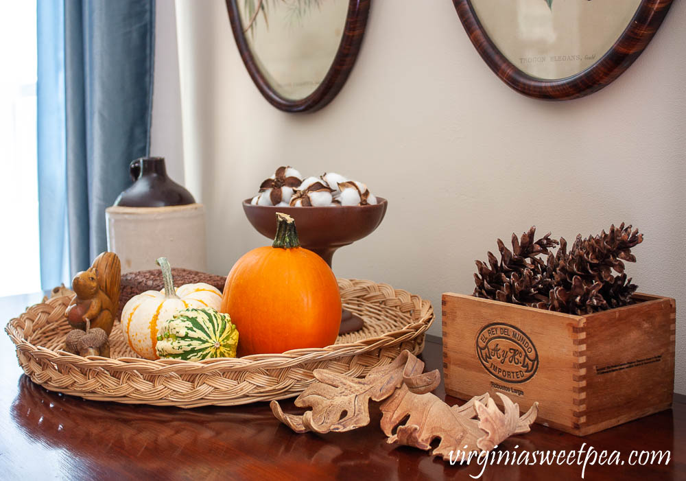 Fall Vignette with an antique jug, handcrafted clay leaves, pumpkins and gourds, a wooden squirrel, wood box from India, a Hagar compote with cotton bolls and a cigar box filled with pinecones