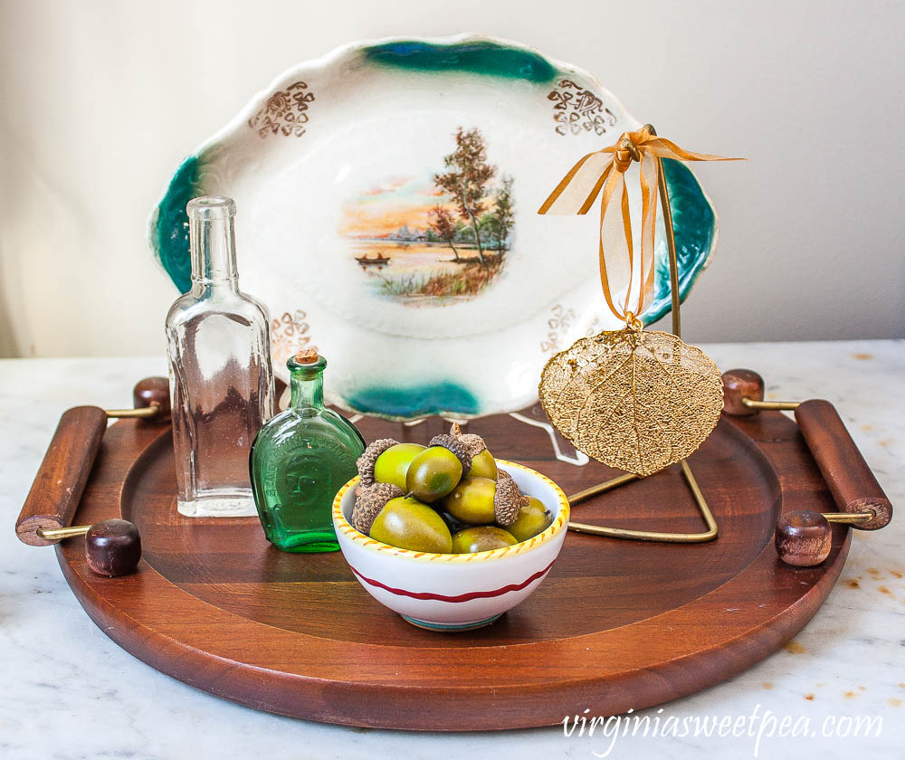 Fall vignette with a small fall plate, vintage bottles, a leaf leaf ornament from Vermont, and a bowl filled with faux acorns