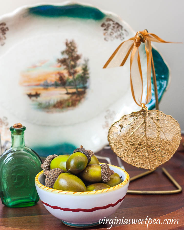 Fall vignette with a small fall plate, vintage bottles, a leaf leaf ornament from Vermont, and a bowl filled with faux acorns