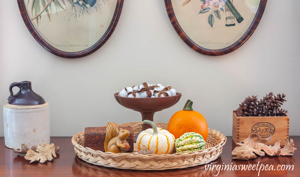 Fall Vignette with an antique jug, handcrafted clay leaves, pumpkins and gourds, a wooden squirrel, wood box from India, a Hagar compote with cotton bolls and a cigar box filled with pinecones