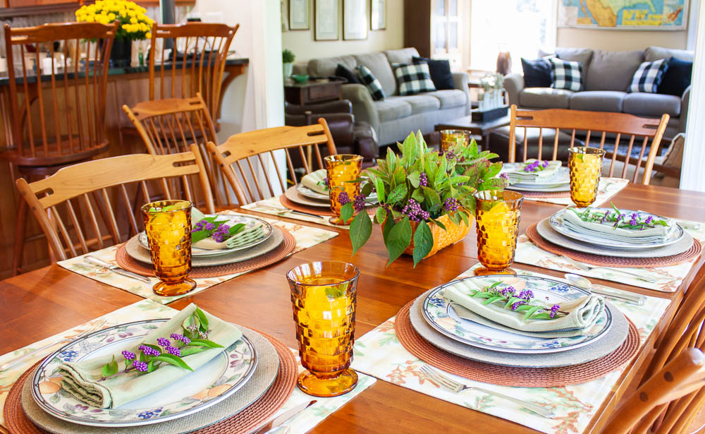 Table set for fall with Mikasa Garden Harvest dishes, vintage amber Anchor Hocking glasses, a centerpiece with Beautyberry and Virginia Sweetspire and layered fall colored placemats and chargers.