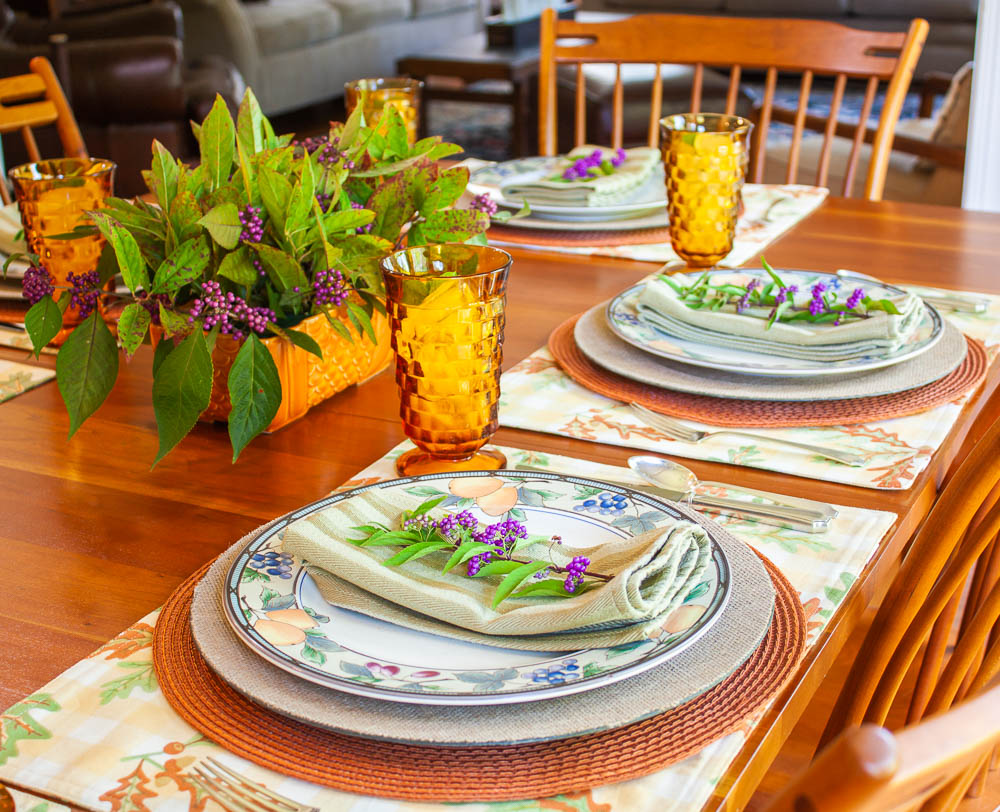 Table set for fall with Mikasa Garden Harvest dishes, vintage amber Anchor Hocking glasses, a centerpiece with Beautyberry and Virginia Sweetspire and layered fall colored placemats and chargers.
