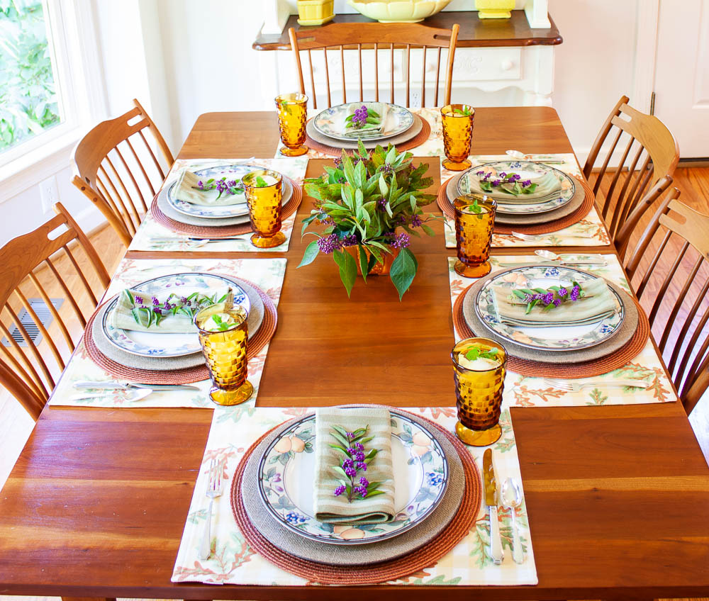 Table set for fall with Mikasa Garden Harvest dishes, vintage amber Anchor Hocking glasses, a centerpiece with Beautyberry and Virginia Sweetspire and layered fall colored placemats and chargers.