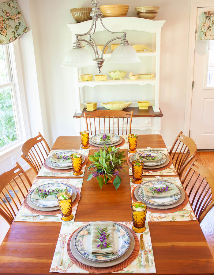 Table set for fall with Mikasa Garden Harvest dishes, vintage amber Anchor Hocking glasses, a centerpiece with Beautyberry and Virginia Sweetspire and layered fall colored placemats and chargers.