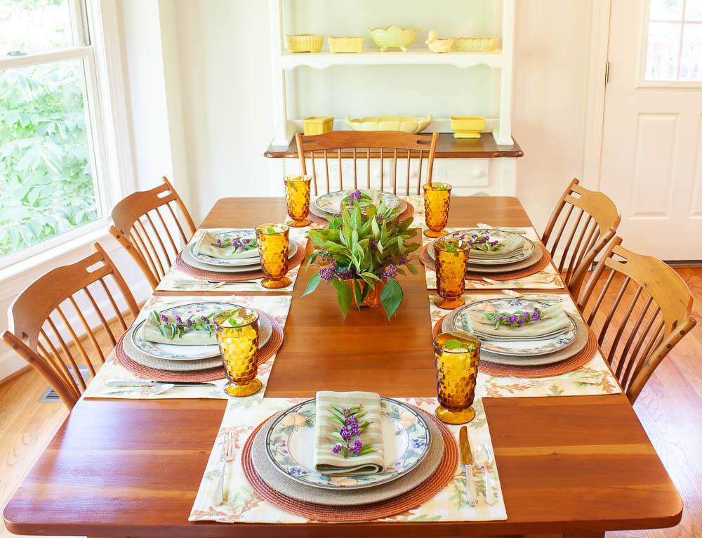 Table set for fall with Mikasa Garden Harvest dishes, vintage amber Anchor Hocking glasses, a centerpiece with Beautyberry and Virginia Sweetspire and layered fall colored placemats and chargers.