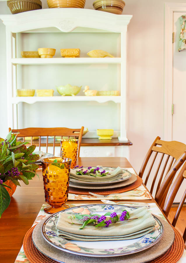 A table set for fall with a painted hutch filled with antique mixing bowls and a collection of yellow vintage flower pots