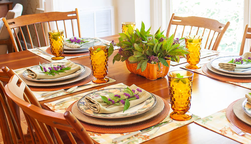 Table set for fall with Mikasa Garden Harvest dishes, vintage amber Anchor Hocking glasses, a centerpiece with Beautyberry and Virginia Sweetspire and layered fall colored placemats and chargers.