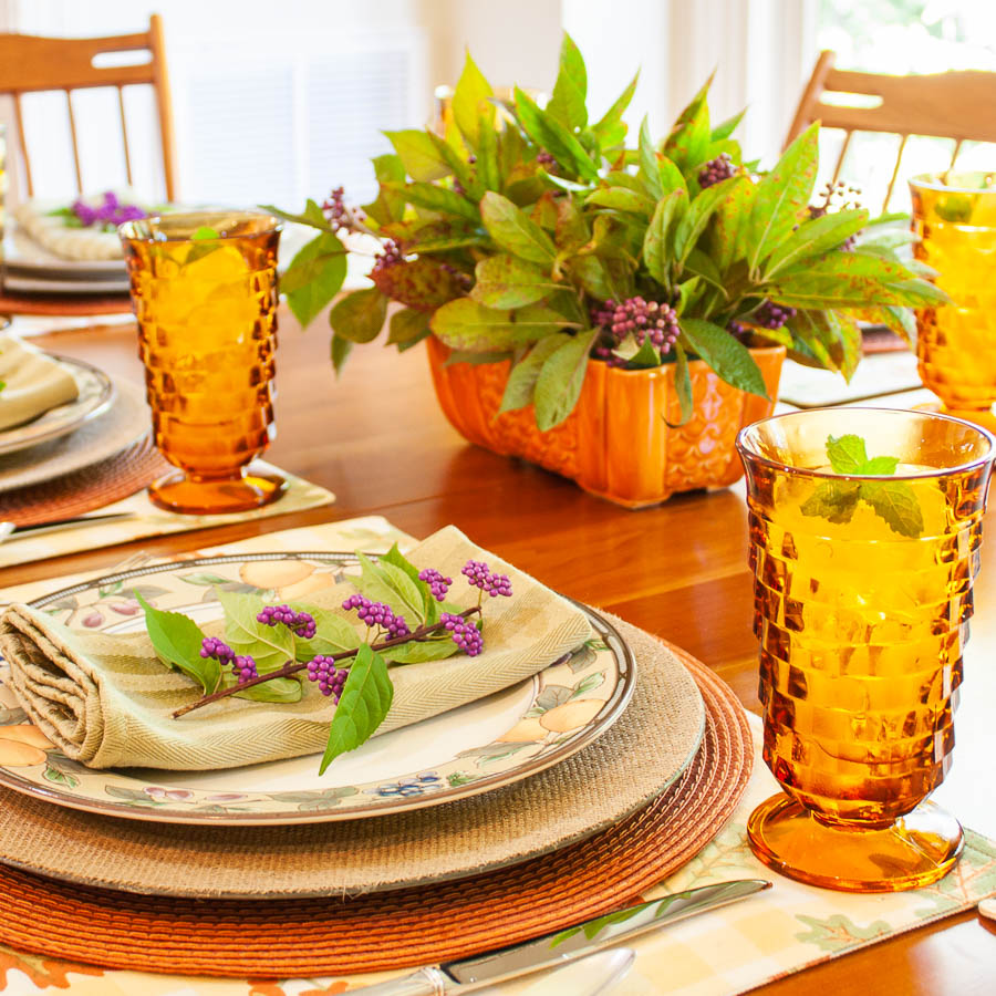 Table set for fall with Mikasa Garden Harvest dishes, vintage amber Anchor Hocking glasses, a centerpiece with Beautyberry and Virginia Sweetspire and layered fall colored placemats and chargers.