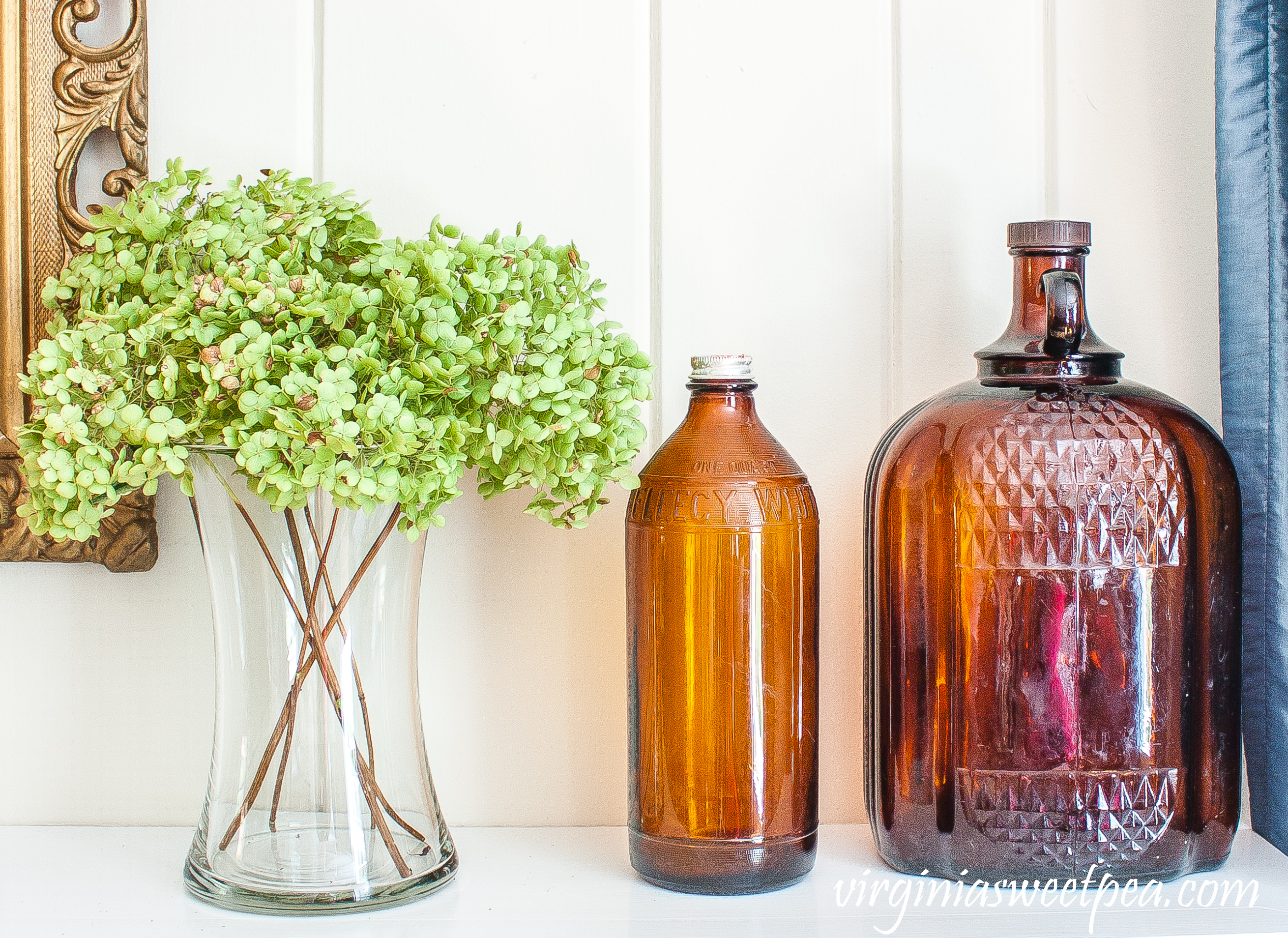 Mantel decorated with Hydrangea in a vase and two vintage brown bottles.