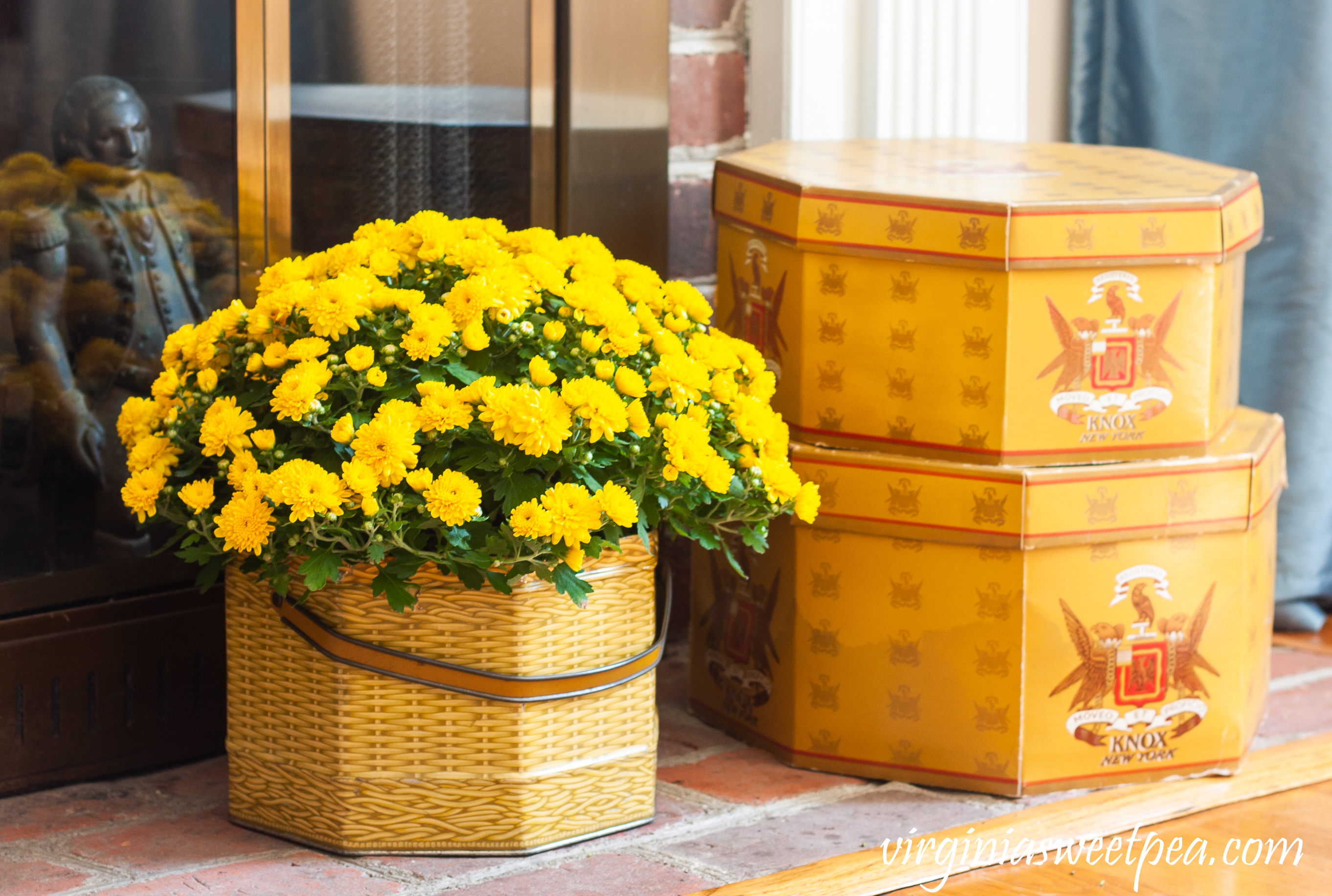Knox New York hat boxes along with a mum in a vintage basket tin decorate a fireplace hearth for fall.