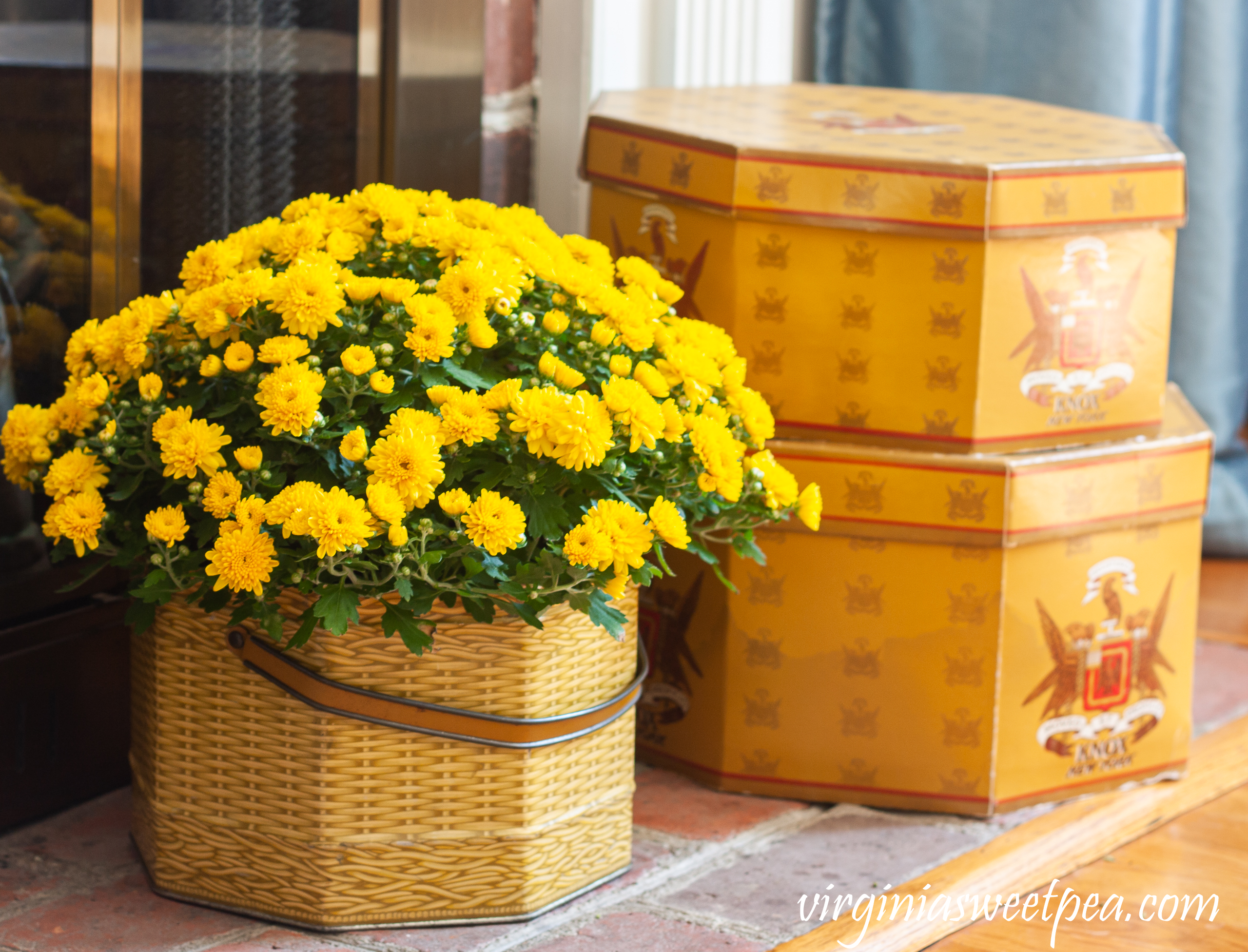 Knox New York hat boxes along with a mum in a vintage basket tin decorate a fireplace hearth for fall.