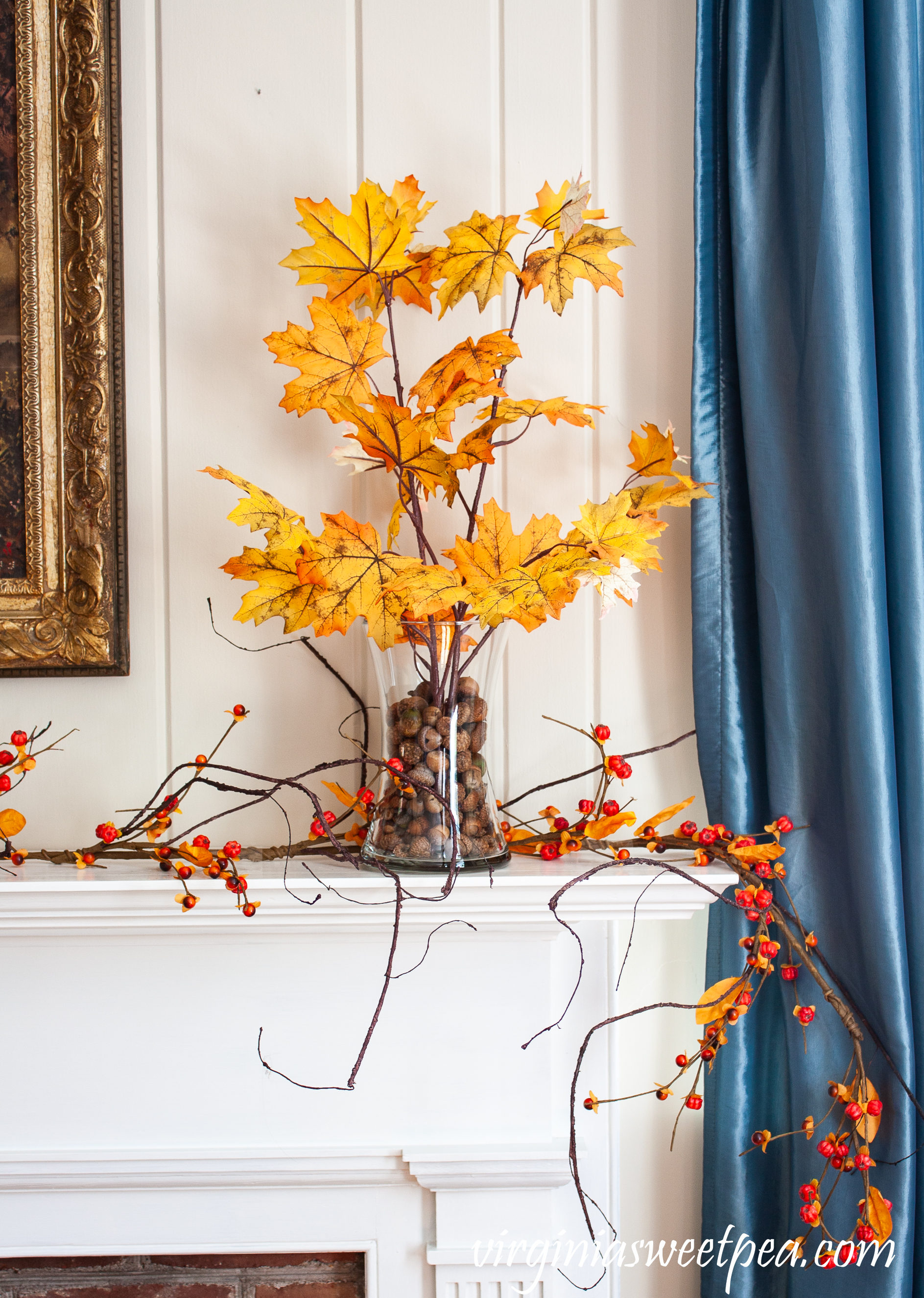 Fall foliage in glass vases anchored with acorns on a mantel with a bittersweet garland