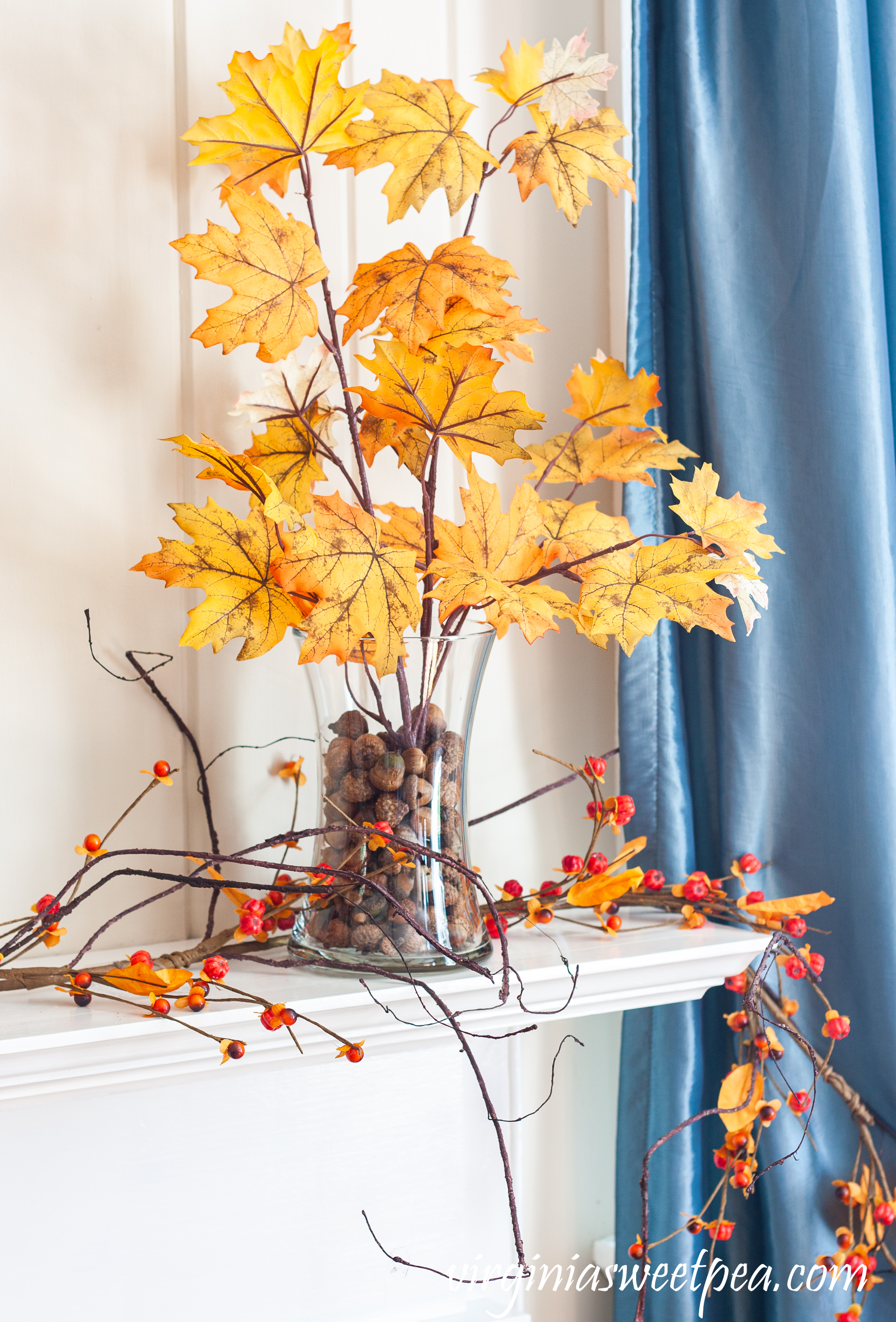 Fall foliage in glass vases anchored with acorns on a mantel with a bittersweet garland