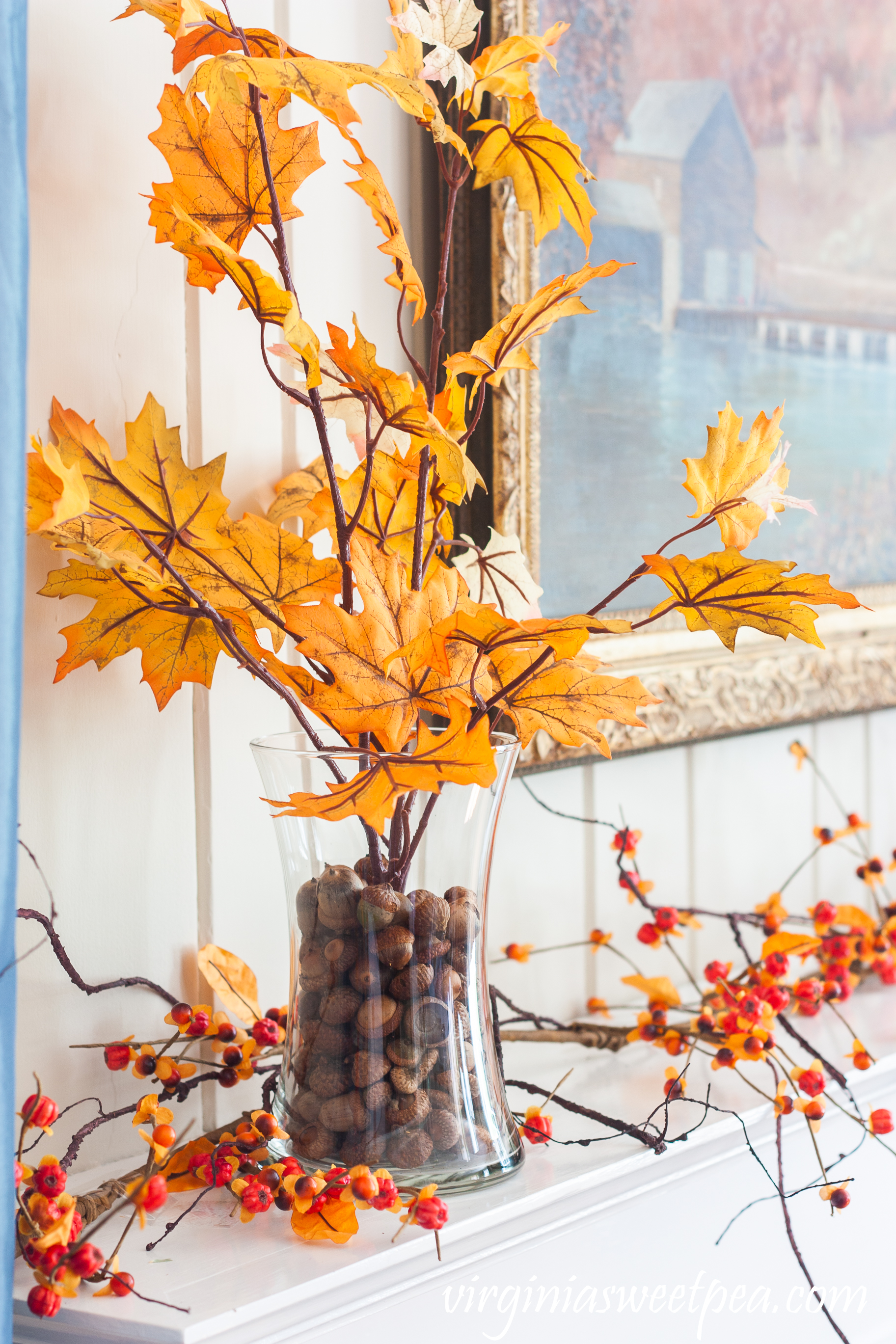 Fall foliage in glass vases anchored with acorns on a mantel with a bittersweet garland