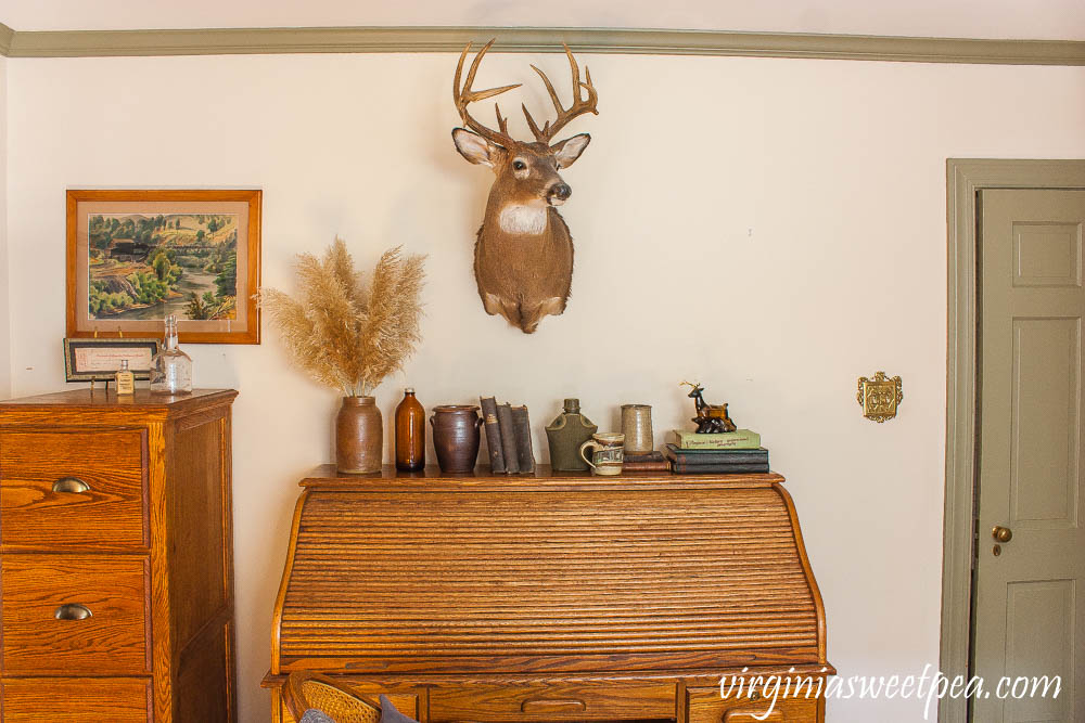 Desk decorated with a cabin theme including a deer head, old books, and pottery.