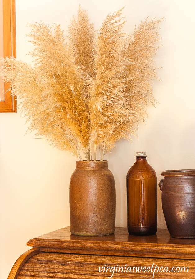 Pampas grass in an antique crock with an amber Fleecy White Clorox bottle and a pottery jar from North Carolina