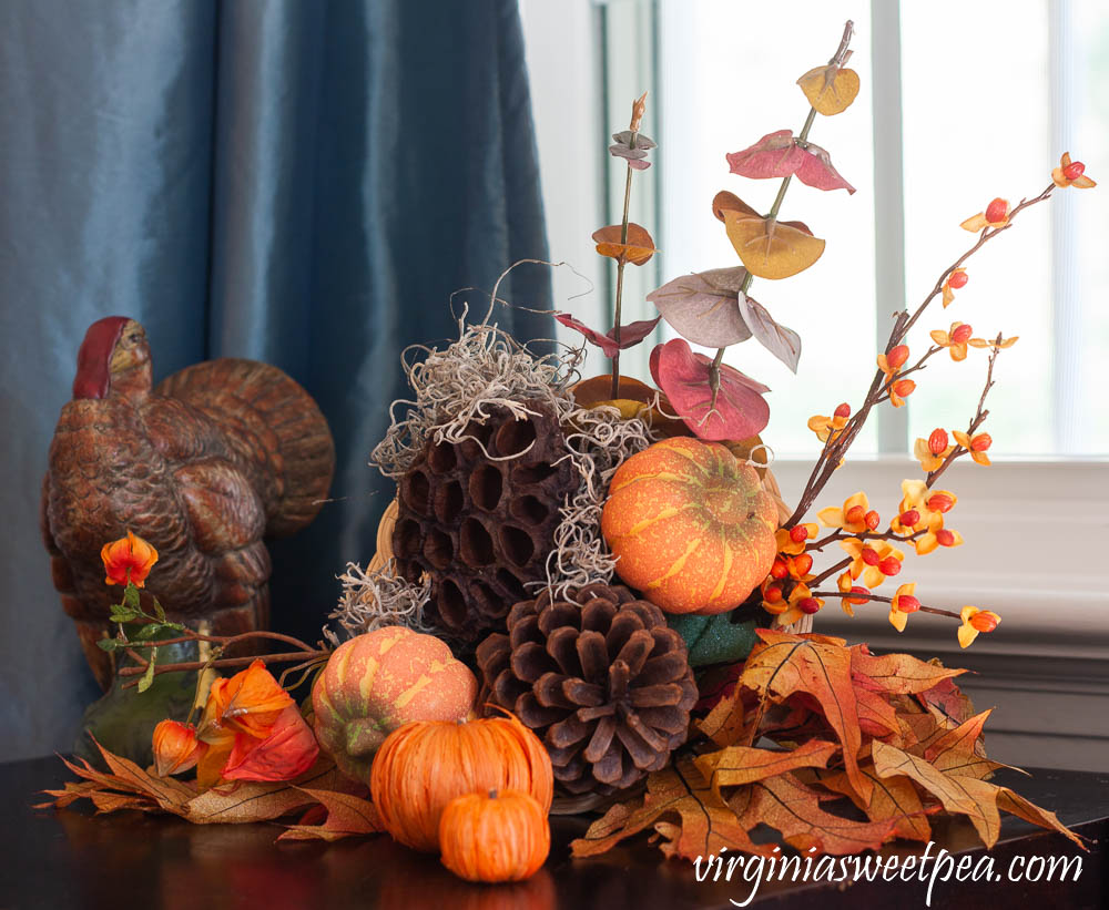 Thanksgiving decor using a turkey figure and a cornucopia filled with bittersweet, japanese lantern, eucalyptus, pumpkins, lotus pods, and pine cones.