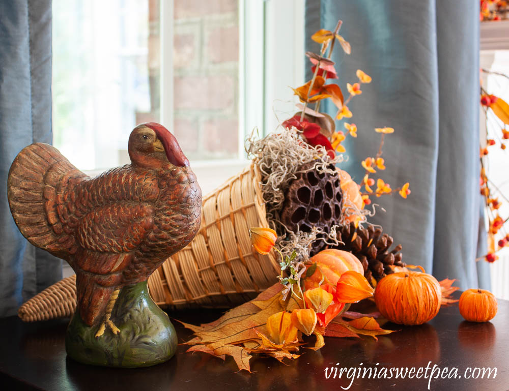 Thanksgiving decor using a turkey figure and a cornucopia filled with bittersweet, japanese lantern, eucalyptus, pumpkins, lotus pods, and pine cones.