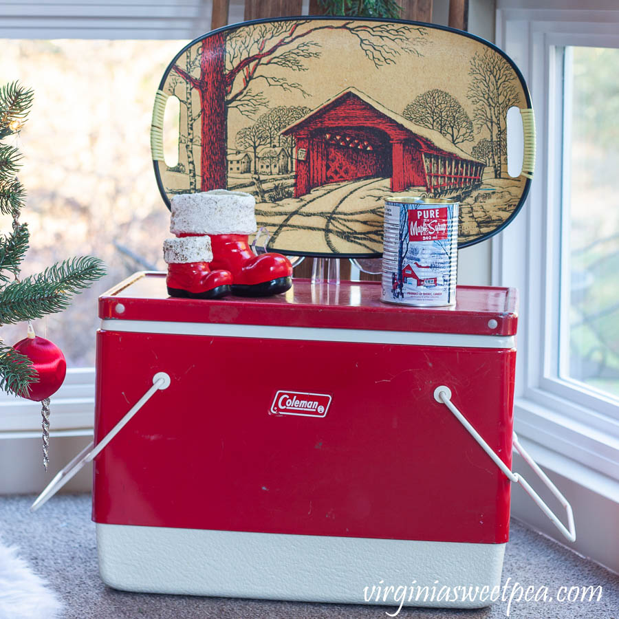 A Very Vintage Christmas on the Porch - Vintage Coleman cooler with vintage Santa boots, a vintage covered bridge tray, and a maple syrup scented candle in a maple syrup can