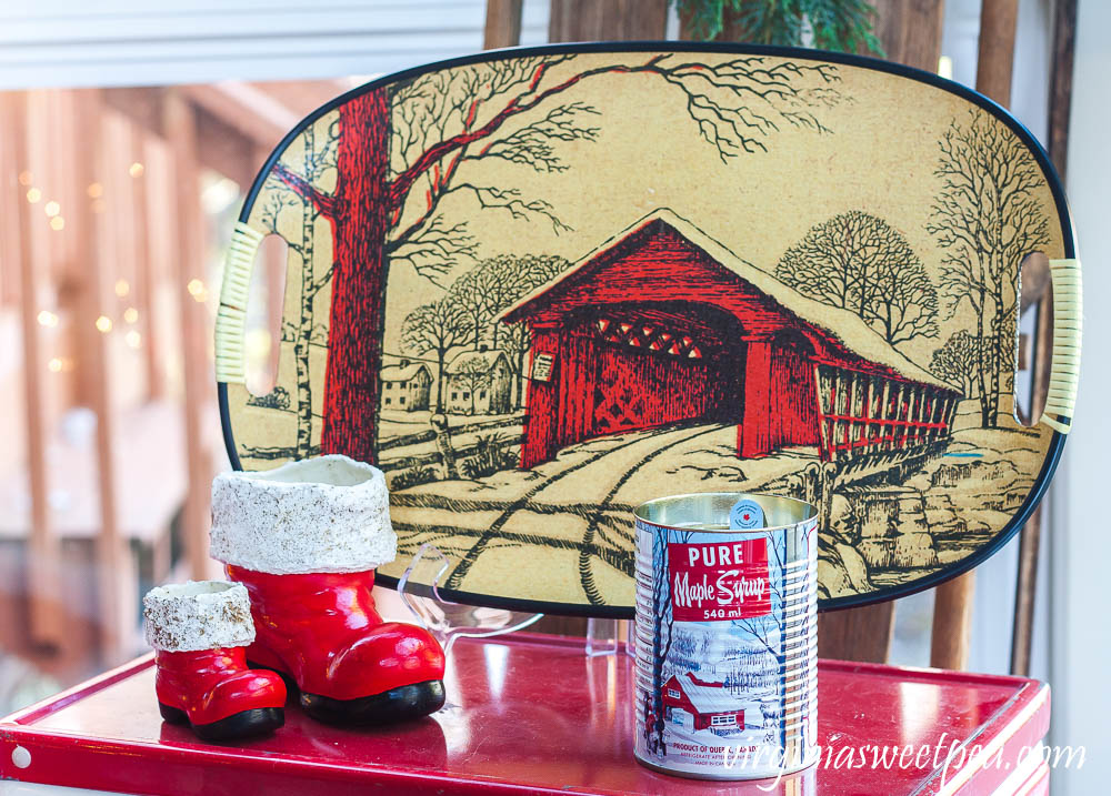 A Very Vintage Christmas on the Porch - Vintage Coleman cooler with vintage Santa boots, a vintage covered bridge tray, and a maple syrup scented candle in a maple syrup can